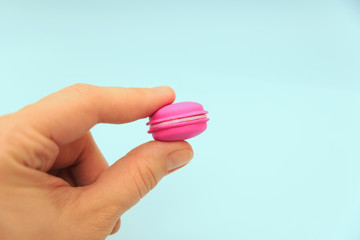 Female fingers hold a pink macaroon on a blue background. Rubber fake, bad imitation	