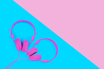 A pair of pink headphones in the shape of a heart on blue background. Summer love music concept with copy space.