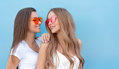 two young hipster woman friends in retro neon sunglasses standing and smiling over blue wall