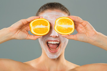 beautiful young woman with a cleansing facial mask with oranges in her hands