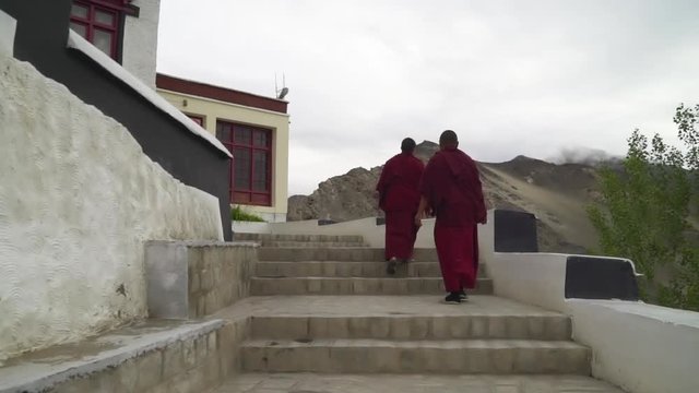 Slow motion handheld tracking shot behind two Tibetan Buddhist monks, as walking up on the stairs at Thiksey Gompa monastery in Ladakh, India, near to Leh