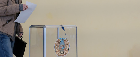 Qazaqstan, 6-9-2019, Elections. A girl in a jacket with a briefcase in the voting room wants to put the ballot in a transparent box with the coat of arms of Kazakhstan. Copy space. Blank for banner.