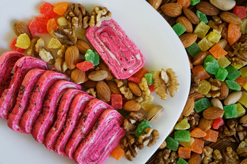Arab sweets: unusual pink halvah in a white plate next to candied fruits, pistachios, almonds and walnuts. National Oriental dishes