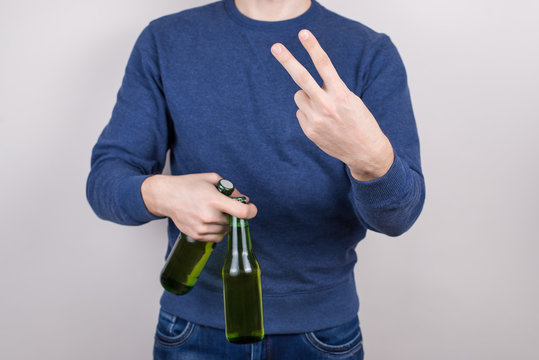 Cropped closeup photo of handsome satisfied positive guy making v-sign symbol to camera holding two fresh beers in palm isolated grey background