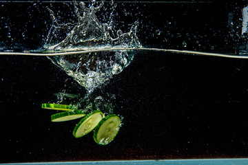 cucumber slices falling in dark water with splashes