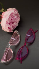 Obraz na płótnie Canvas pink peony and pink glasses on a wooden table, pink sun glasses, stylish glasses (vertically)