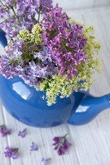 Lilac in a teapot of blue color with a place for an inscription on a wooden background. Lilac flowers