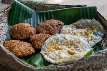 Crispy deep fired vadai snack and omelet on a banana leaf in a knitted basket. Sri Lankan breakfast.