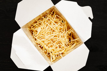 Dry noodles in paper box on a black table, top view
