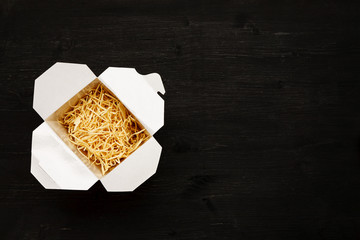 Dry noodles in paper box on a black table, top view, text space