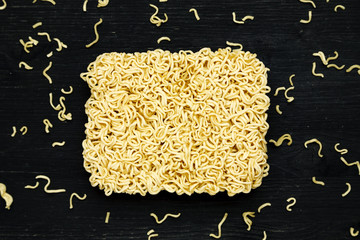 Briquet of instant noodles on a black wooden table, close-up, top view