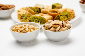 Pine nut and pistachio in ceramic bowls with traditional oriental sweets in the background