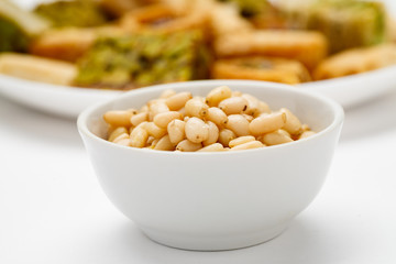 Pine nut in ceramic bowl with traditional oriental sweets in the background, close-up