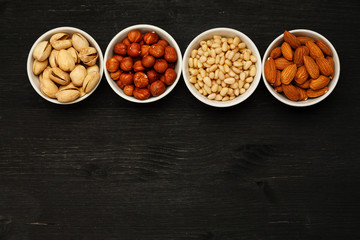 Different nuts in ceramic bowls on a black wooden table, top viev, text space