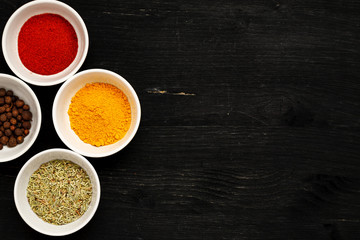Different spices in ceramic bowls on a black wooden table, top view, text space