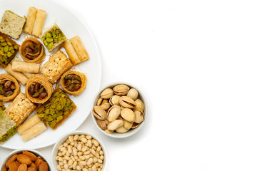 Traditional oriental sweets in white plate with different nuts on a white table, top view, copy space