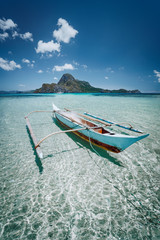 Small fishing banca boat in front of Cadlao Island in crystal clear shallow water, low tide, amazing nature of Palawan, Philippines