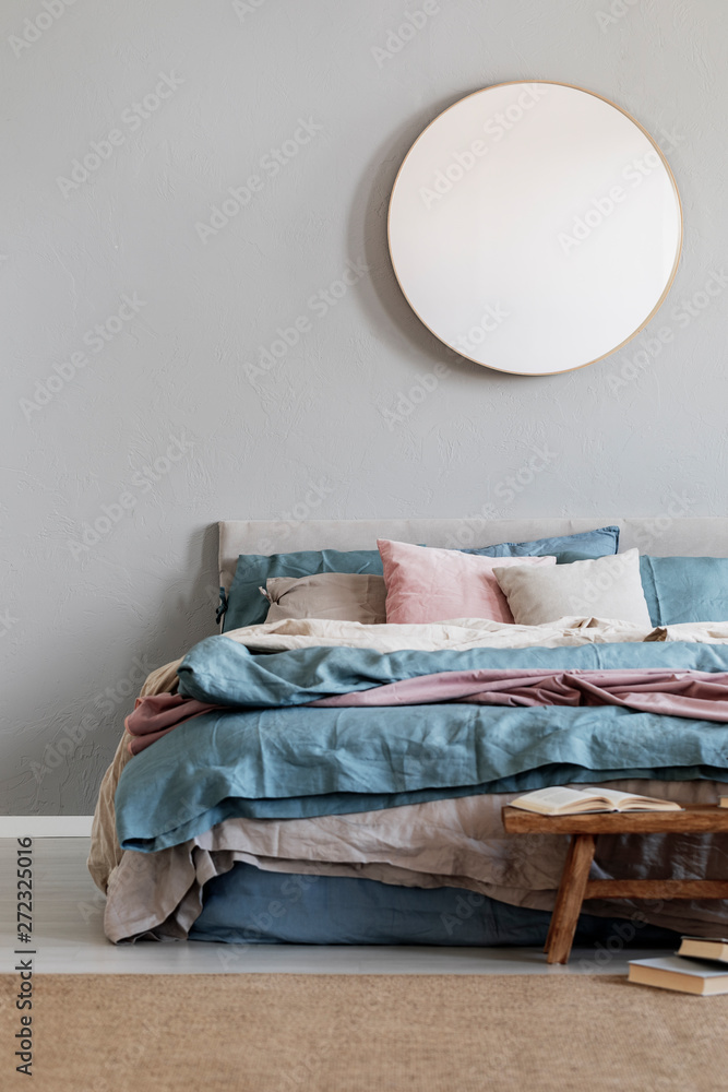 Wall mural Classy round mirror on grey wall in stylish bedroom interior with warm bed with blue, pastel pink and beige bedding