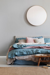 Classy round mirror on grey wall in stylish bedroom interior with warm bed with blue, pastel pink and beige bedding