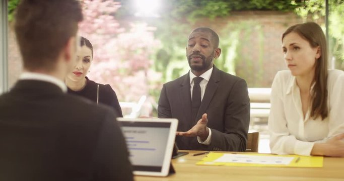 4K Businessman being told he's losing his job in a meeting with uncaring management team. Slow motion.