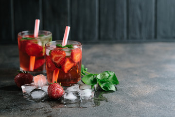 Fresh summer strawberry lemonade with basil and ice on a dark background copy space.
