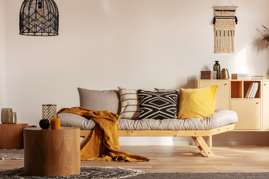 Scandinavian Sofa With Pillows And Dark Yellow Blanket In Bright Living Room Interior With Black Chandelier