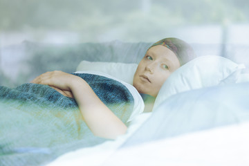 Thoughtful woman battling with tumor lying in hospice bed