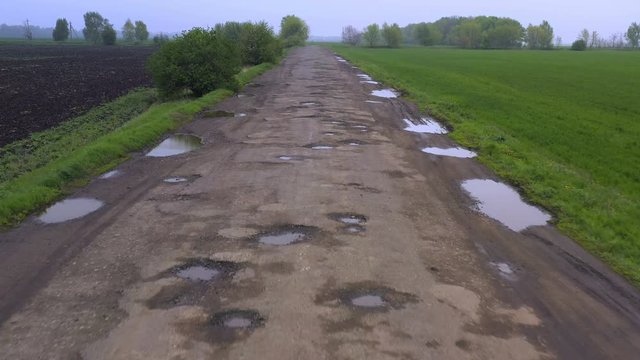 bad rural road with the lot of pits holes and puddles after the rain