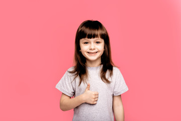 Ready to school. Cheerful little girl looking up with smile while standing against pink background. Education, gesture and school concept - happy and smiling confident little girl showing finger up