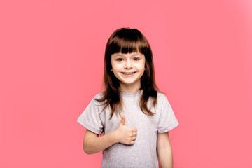 Fototapeta premium Ready to school. Cheerful little girl looking up with smile while standing against pink background. Education, gesture and school concept - happy and smiling confident little girl showing finger up
