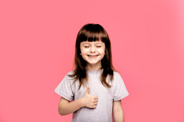 Fototapeta premium Young emotional little girl showing finger up gesture and her respect for something, portrait child over pink studio background. Human emotions, lifestyle, freestyle, smile, blank, funny gesture.