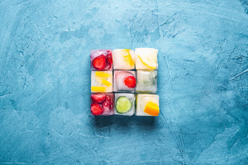 Ice cubes with fruit on a stone blue background. The shape of the square. Mint, strawberry, cherry,...