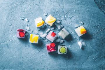 Ice cubes with fruit and broken ice on a stone blue background. Mint, strawberry, cherry, lemon, orange. Flatlay, top view