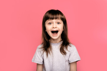 Wow. Crazy good news. Image of overjoyed excited screaming amazed little child girl standing isolated over pink background. Looking camera with open mouth. 