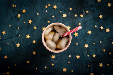 Iced coffee in a glass on a dark blue stone background with stars. Concept cooling drink, thirst, summer, cola with ice, night life, club. Flat lay, top view