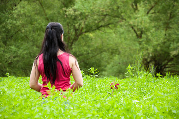 A woman in a burgundy shirt stands among the high green grass and plants. Summer in the garden. Tall trees