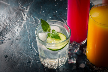 Four kinds of refreshing drinks with ice on a dark blue background and ice cubes. Concept night club, night life, party, thirst. Orange, mint and cucumber, strawberry, cola. Flat lay, top view