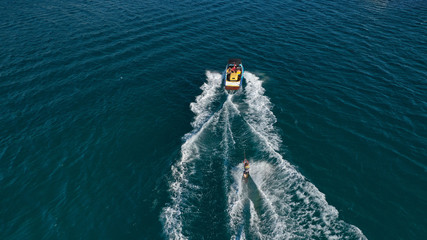Aerial photo of man practicing high speed water ski towed by speed boat in deep blue sea