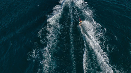 Aerial photo of man practicing high speed water ski towed by speed boat in deep blue sea
