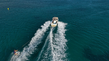 Aerial photo of man practicing high speed water ski towed by speed boat in deep blue sea