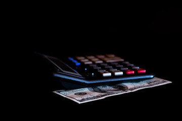 Expenses cost, budget and tax or investment calculation, one hundred dollar with calculator on dark black background table with blank copy space.