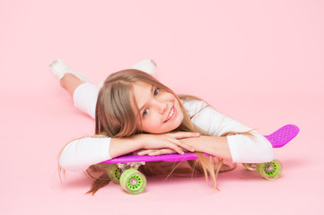 Obraz na płótnie Canvas Spreading happy vibrations with the penny board. Small girl skater relaxing at penny board deck on pink background. Little child smiling with violet penny board. Happy hipster with penny skateboard