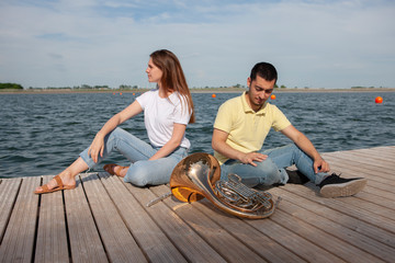 The guy playing the horn and the girl playing the flute on the lake