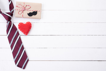 Happy fathers day concept. Top view of blue tie, beautiful gift box, red heart with man mustache on white wooden table background. Flat lay.