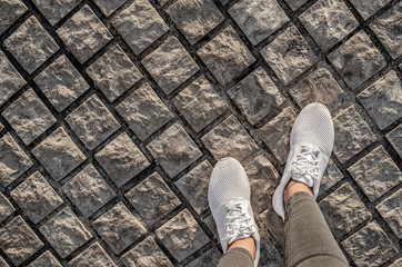 Women's legs in white sneakers on the pavement.