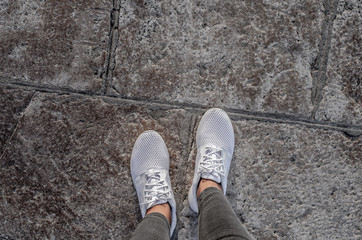 Women's legs in white sneakers on the pavement.