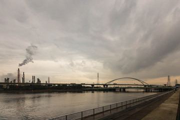 Smokestack emits gas into sunset sky next to waterway