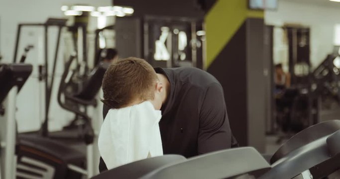 Tired sportsmen removes a towel from his shoulder and wipes his face after training
