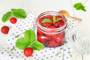 Delicious strawberry jam in traditional glass jar on white wooden background