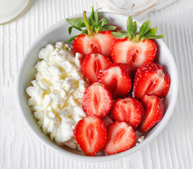 White bowl with fresh red ripe strawberries and natural cottage cheese